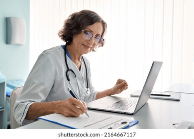 Senior Middle Aged Female Medical Worker In Modern Clinic Wearing White Doctors Coat Having Videocall Using Laptop Writing Health Personal Data Consulting Remotely Telemedicine Healthcare Concept