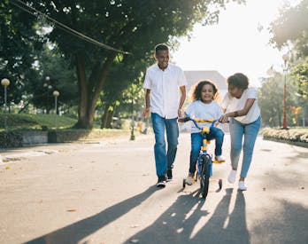 Man Standing Beside His Wife Teaching Their Child How To Ride Bicycle